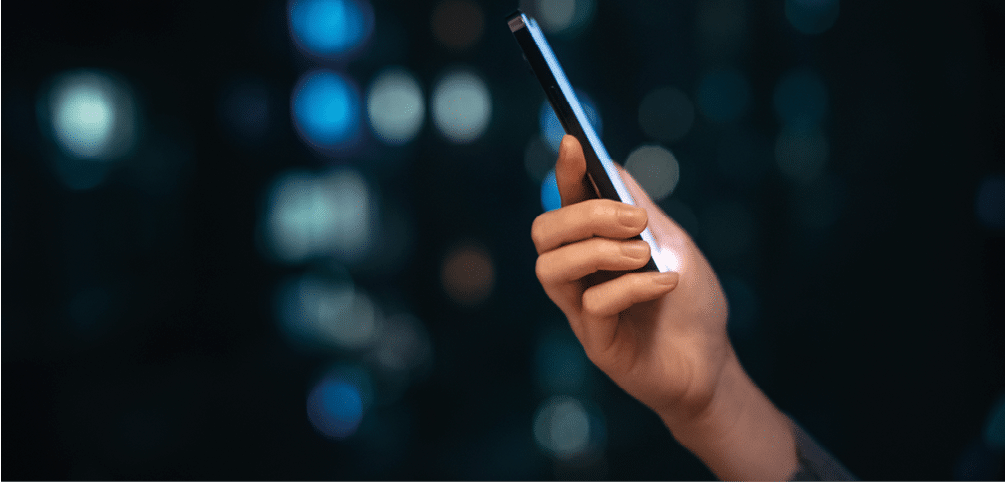 Close up shot of female hand using smartphone at night, against illuminated and defocused bokeh in background. Lifestyle and technology